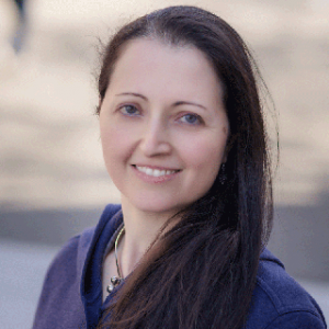 Anat CaspiA white woman smiling into the camera. She is wearing a purple blouse.