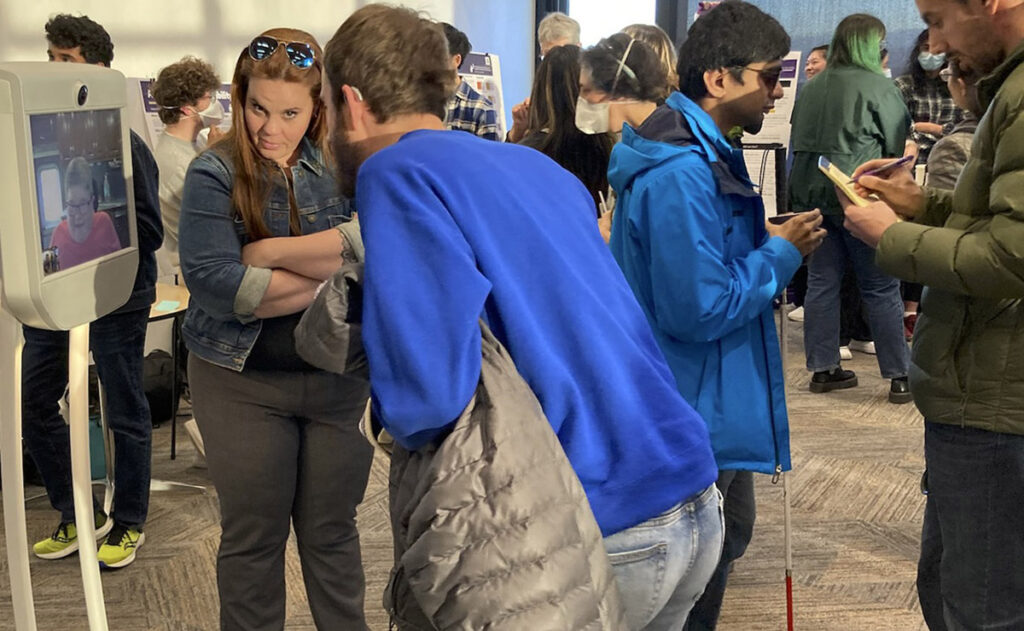 Devin Meyers, representing CREATE community partner Hearing, Speech and Deaf Center, converses with a remote attendee via mobile screen and an ASL interpreter.